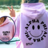 A girl wearing a pink hoodie with a logo of Alpha PHI